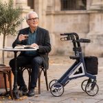Älterer Herr im Straßencafé mit dem geparkten Rollator Alevo Alu in Nachtblau
