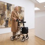 Elegante ältere Dame mit dem Rollator Alevo Alu in Platin in einer Kunstgalerie