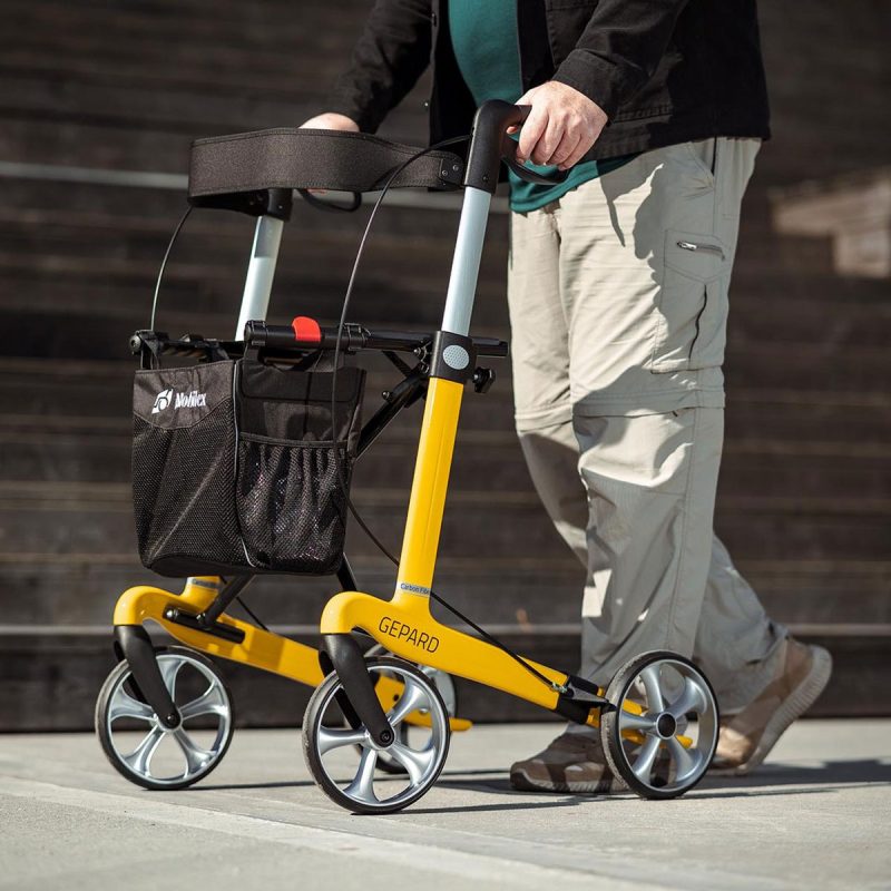 Mann geht mit dem gelben Carbon-Rollator Gepard über eine Holzpromenade